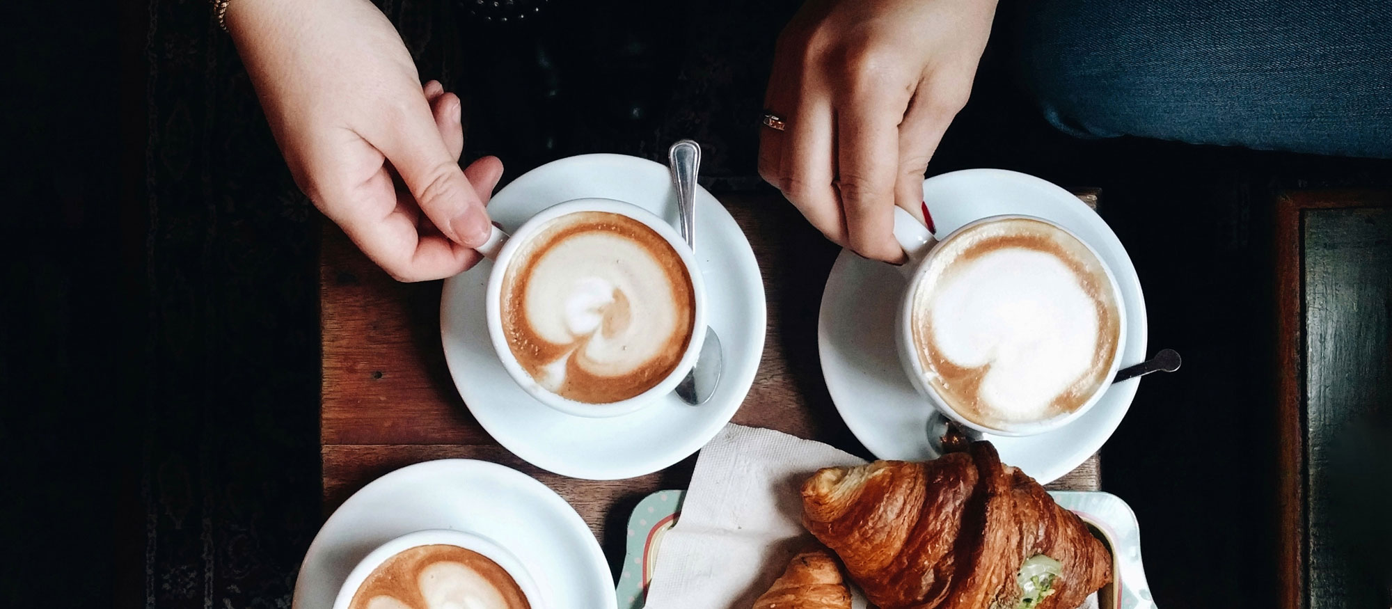 Tre personer sitter på ett café och fikar fikar kaffe latte och croissanter